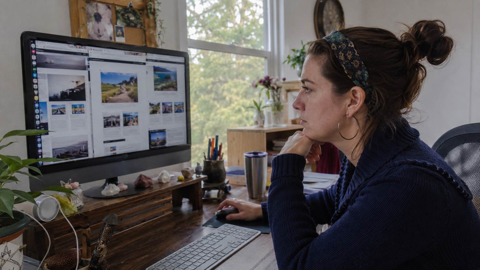 Femme au bandeau fleuri et pull bleu marine consultant des pages web sur un iMac argenté dans un bureau lumineux